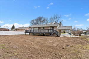 Expansive backyard space featuring a large wooden deck with dark railings, a white privacy fence, and a covered carport with a concrete pad