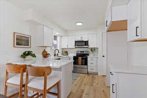 Bright kitchen featuring white cabinetry, light-toned wood-finish flooring, stainless steel appliances, and white countertops