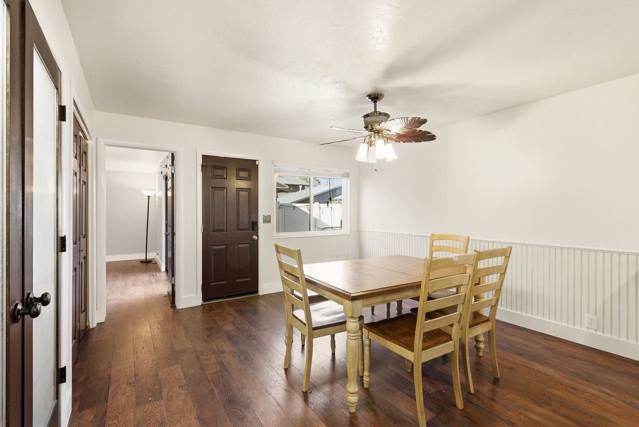 Dining area with dark wood finished floors, a ceiling fan, and wainscoting