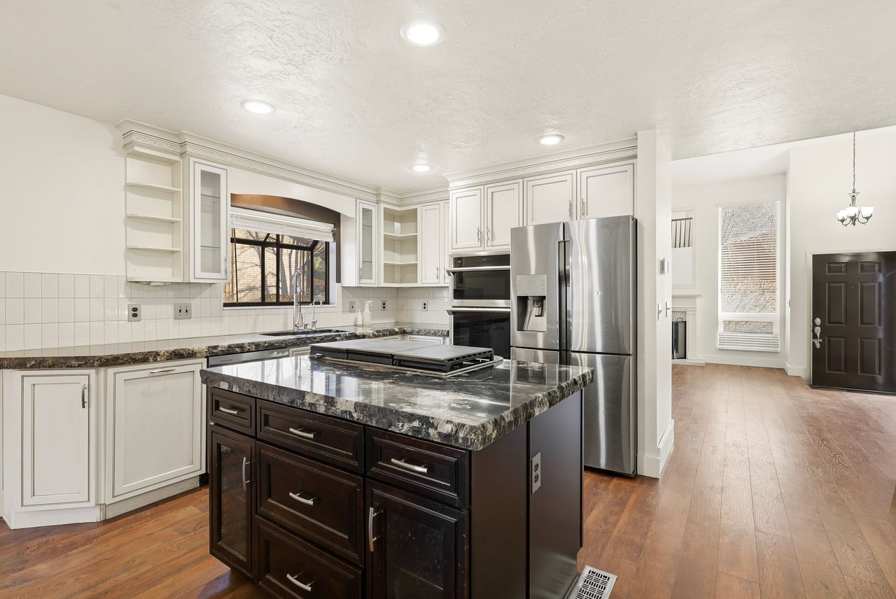 Two tone kitchen featuring two tone color scheme, stainless steel appliances, a kitchen island, dark wood-type flooring, and dark stone counters