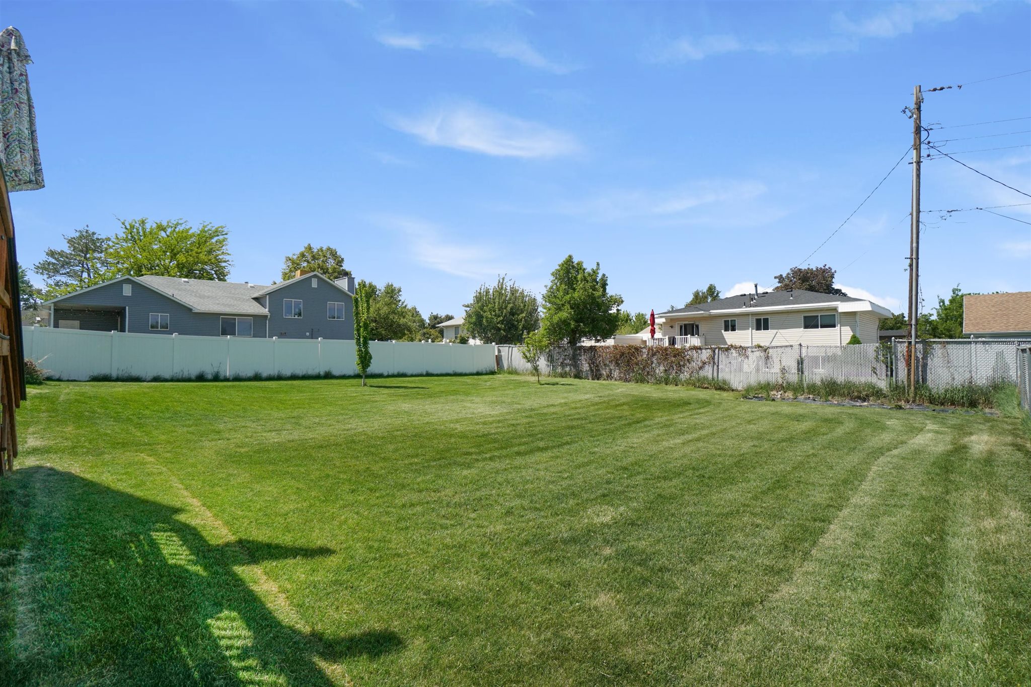 Expansive backyard featuring a manicured lawn, a full perimeter fence, and mature trees