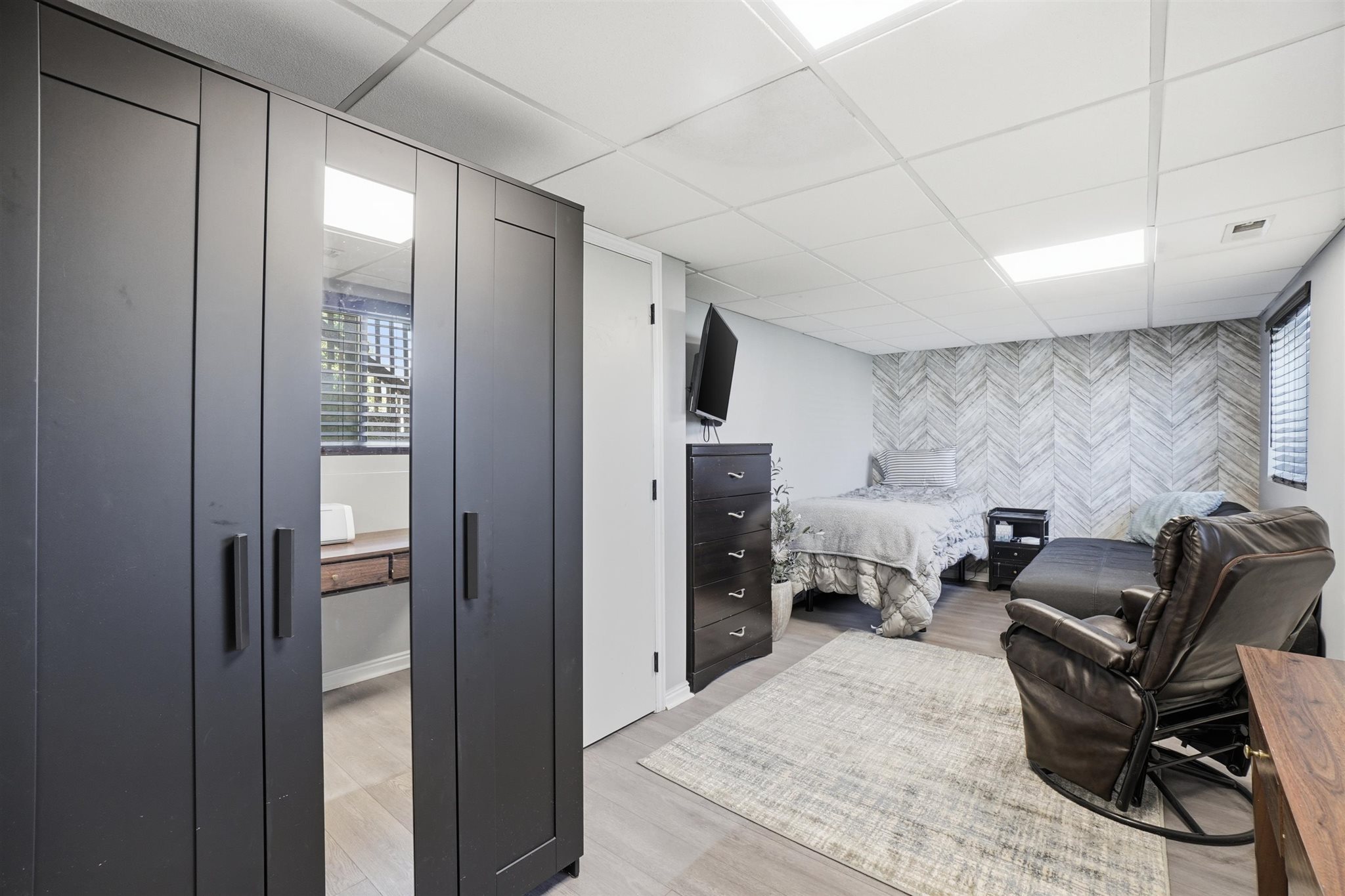 Spacious room featuring light wood-finish flooring, a decorative accent wall, white walls, and a dropped ceiling with integrated lighting