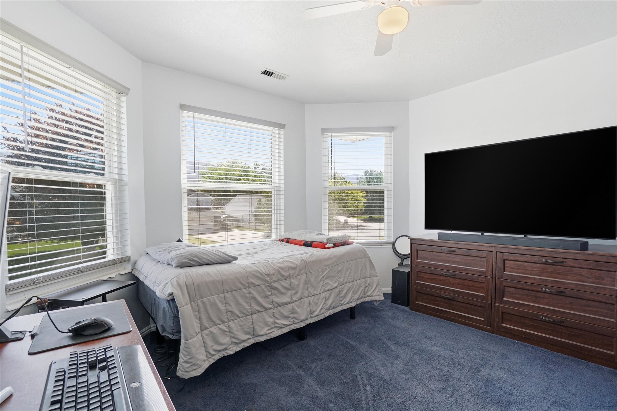 Carpeted room featuring a ceiling fan with integrated lighting, multiple windows with blinds, and a built-in dark wood-finish dresser