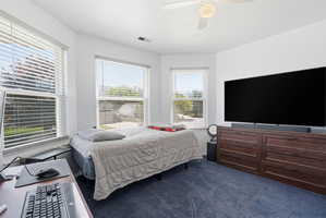 Carpeted room featuring a ceiling fan with integrated lighting, multiple windows with blinds, and a built-in dark wood-finish dresser