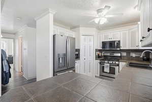Well-appointed kitchen featuring white cabinetry, stainless steel appliances, a tile backsplash, and a ceiling fan