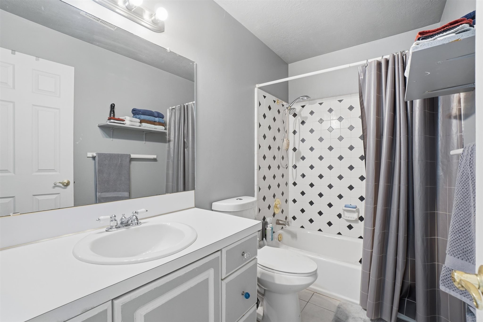 Bathroom featuring a white vanity with an integrated sink, a large wall-mounted mirror, and a three-bulb vanity light fixture