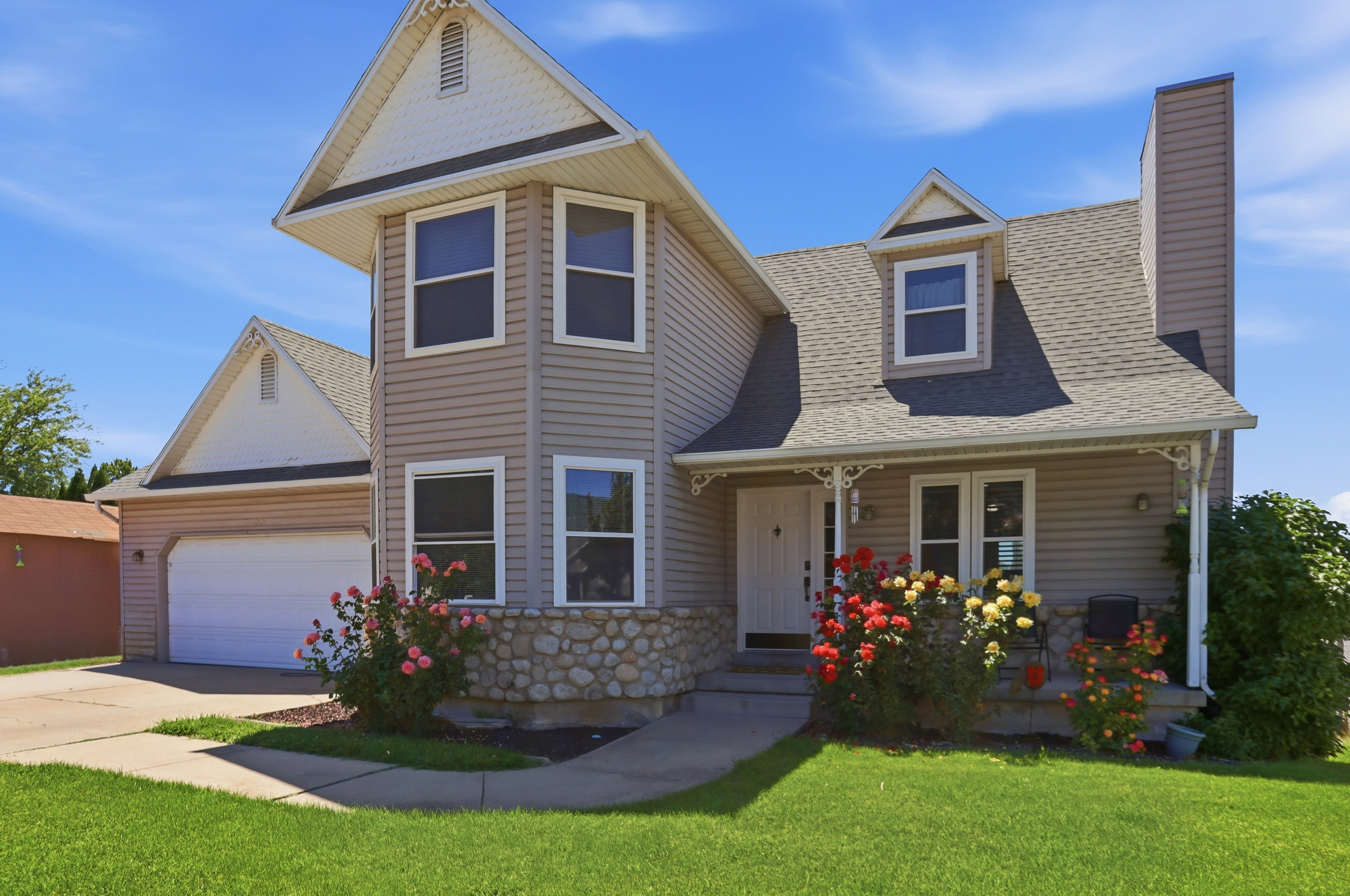 Exterior facade featuring a two-car garage, dormer window, front porch with decorative railing, stone foundation accents, and a bay window