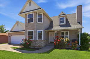 Exterior facade featuring a two-car garage, dormer window, front porch with decorative railing, stone foundation accents, and a bay window