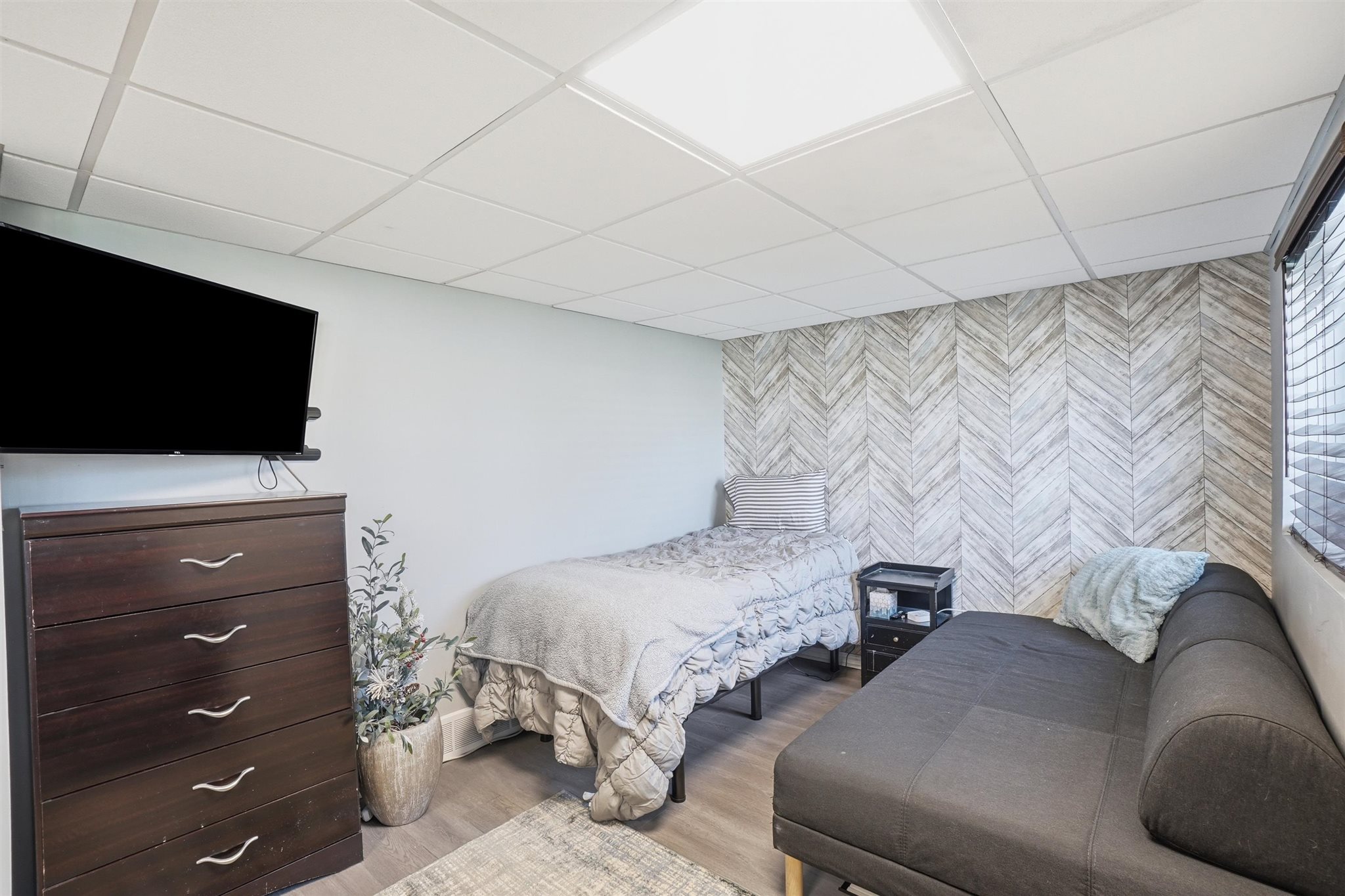 Herringbone pattern accent wall featuring wood-finish flooring, a suspended ceiling, and window blinds