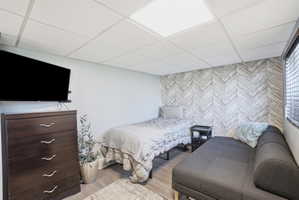 Herringbone pattern accent wall featuring wood-finish flooring, a suspended ceiling, and window blinds
