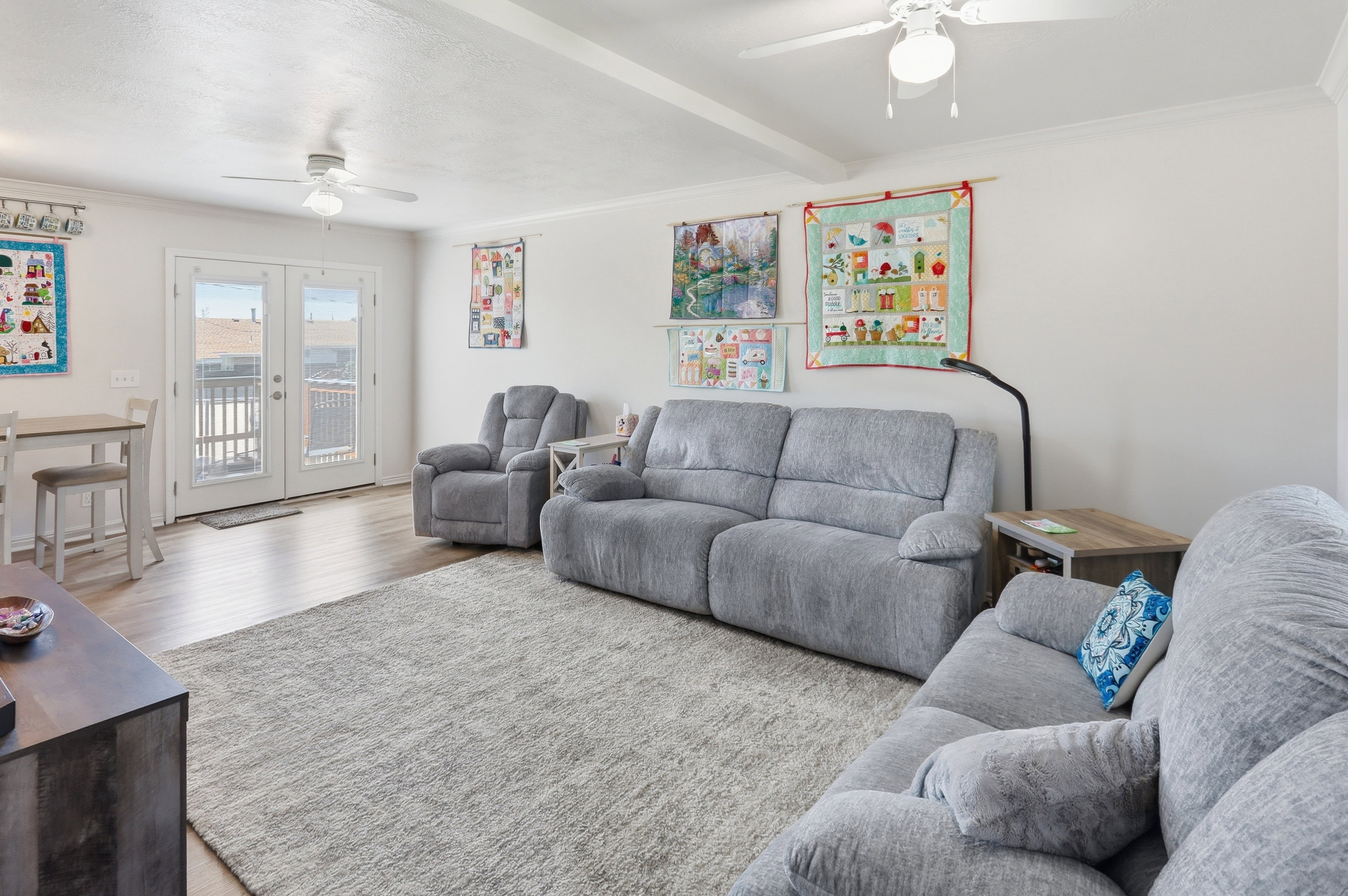 Spacious living area featuring wood-finish flooring, two ceiling fans with integrated lighting, and crown molding