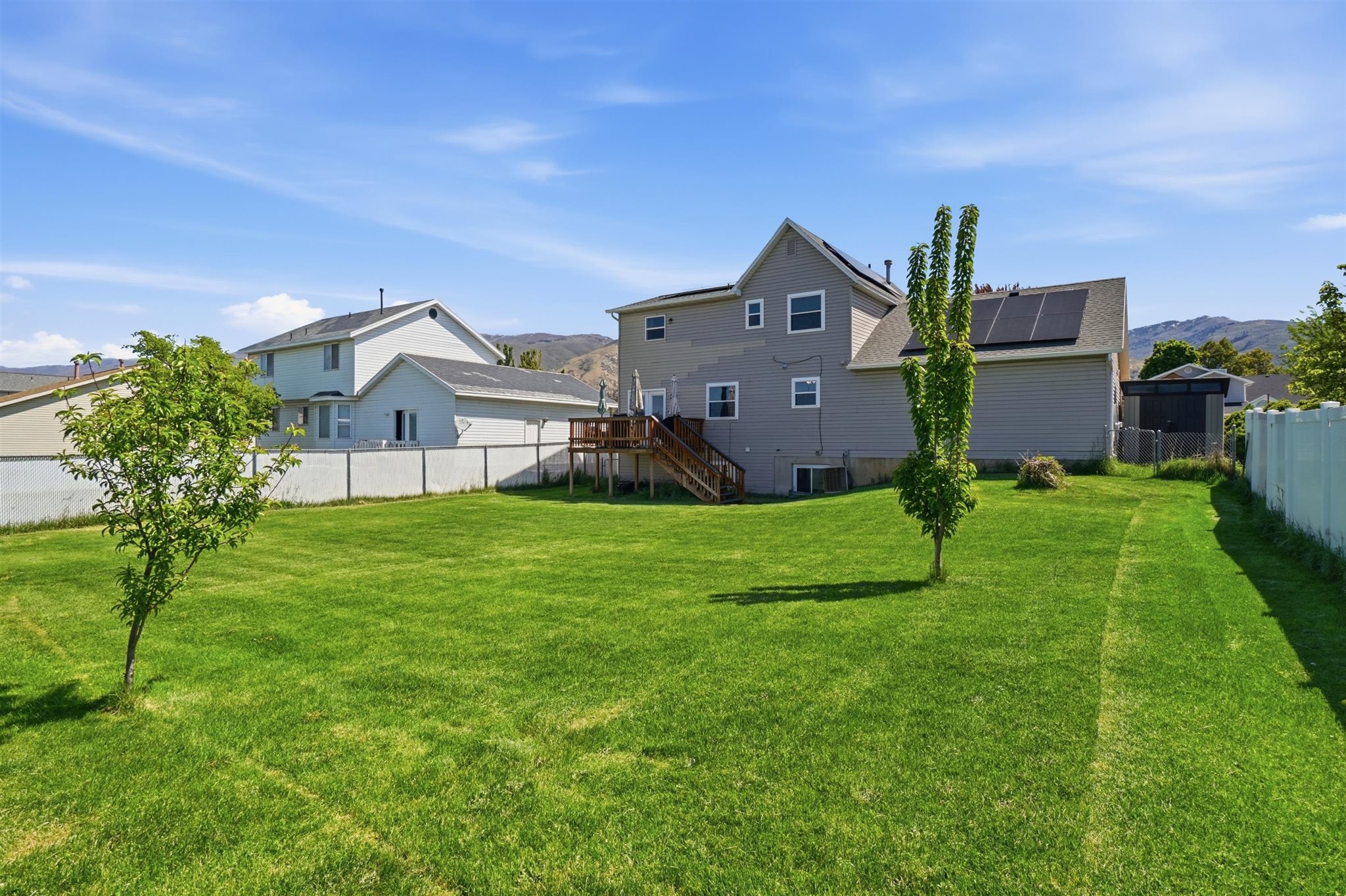 Expansive green lawn with established trees, a white vinyl fence, and a multi-level deck