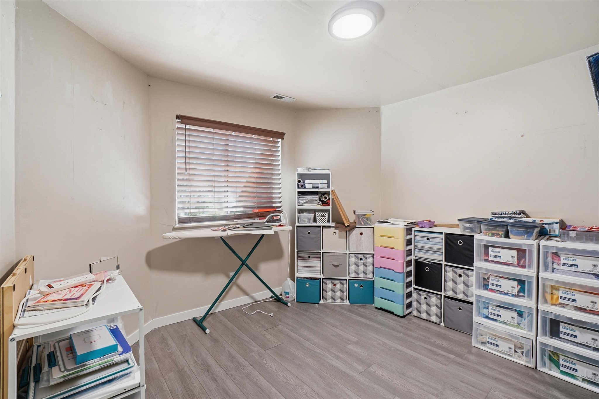 Spacious room featuring wood-finish flooring, a window with blinds, and a flush-mount ceiling light