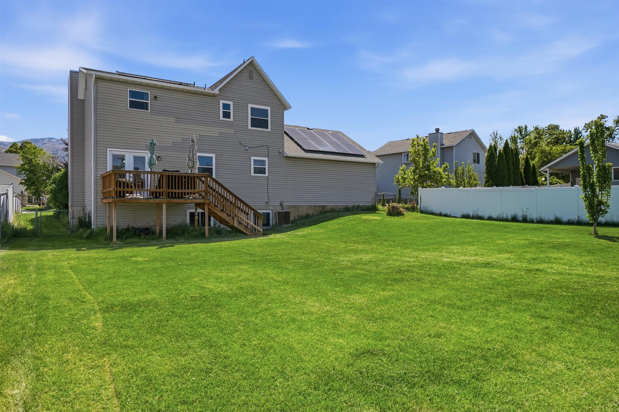 Spacious rear lawn with a full wooden deck and stairs