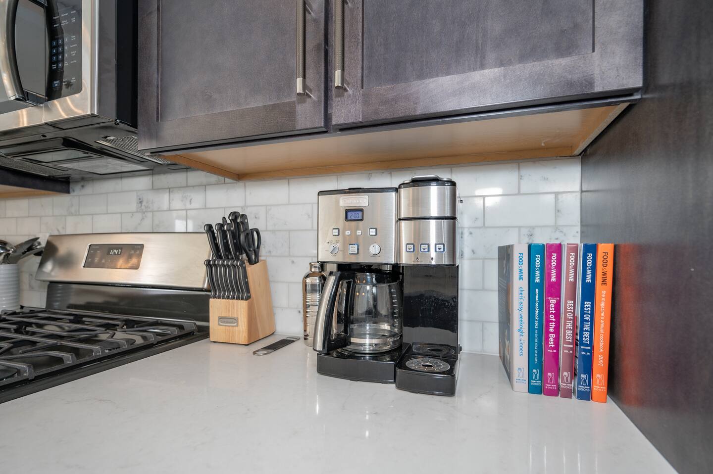 Kitchen view of dark wood finish cabinets, stainless steel appliances, backsplash, and light stone countertops