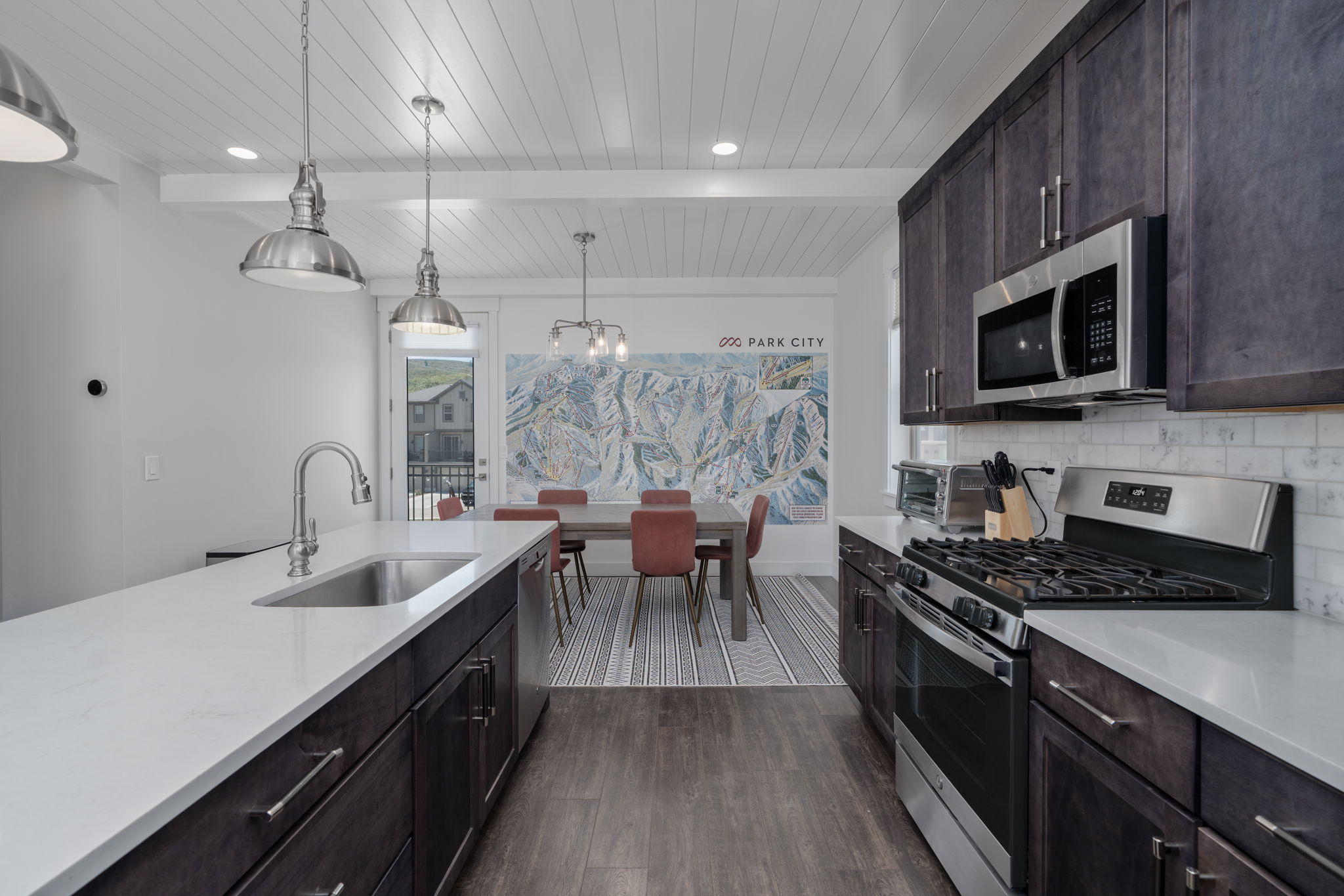 Kitchen featuring dark wood finish cabinetry, stainless steel appliances, dark wood-type flooring, hanging light fixtures, and a wood ceiling with exposed beams