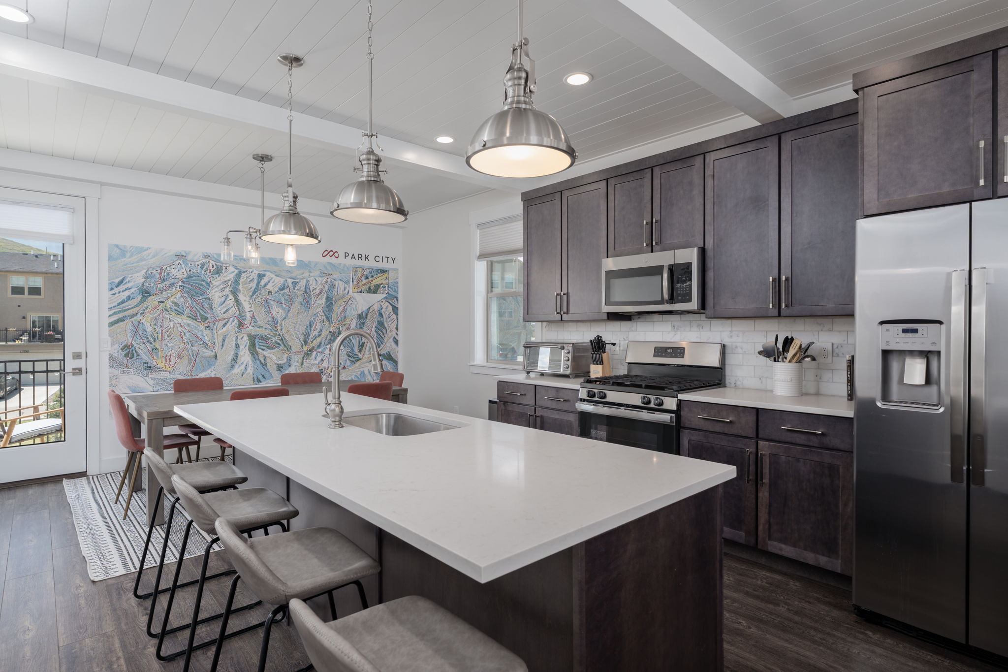 Kitchen featuring dark wood finish cabinetry, stainless steel appliances, a breakfast bar, pendant lighting, and an island with sink