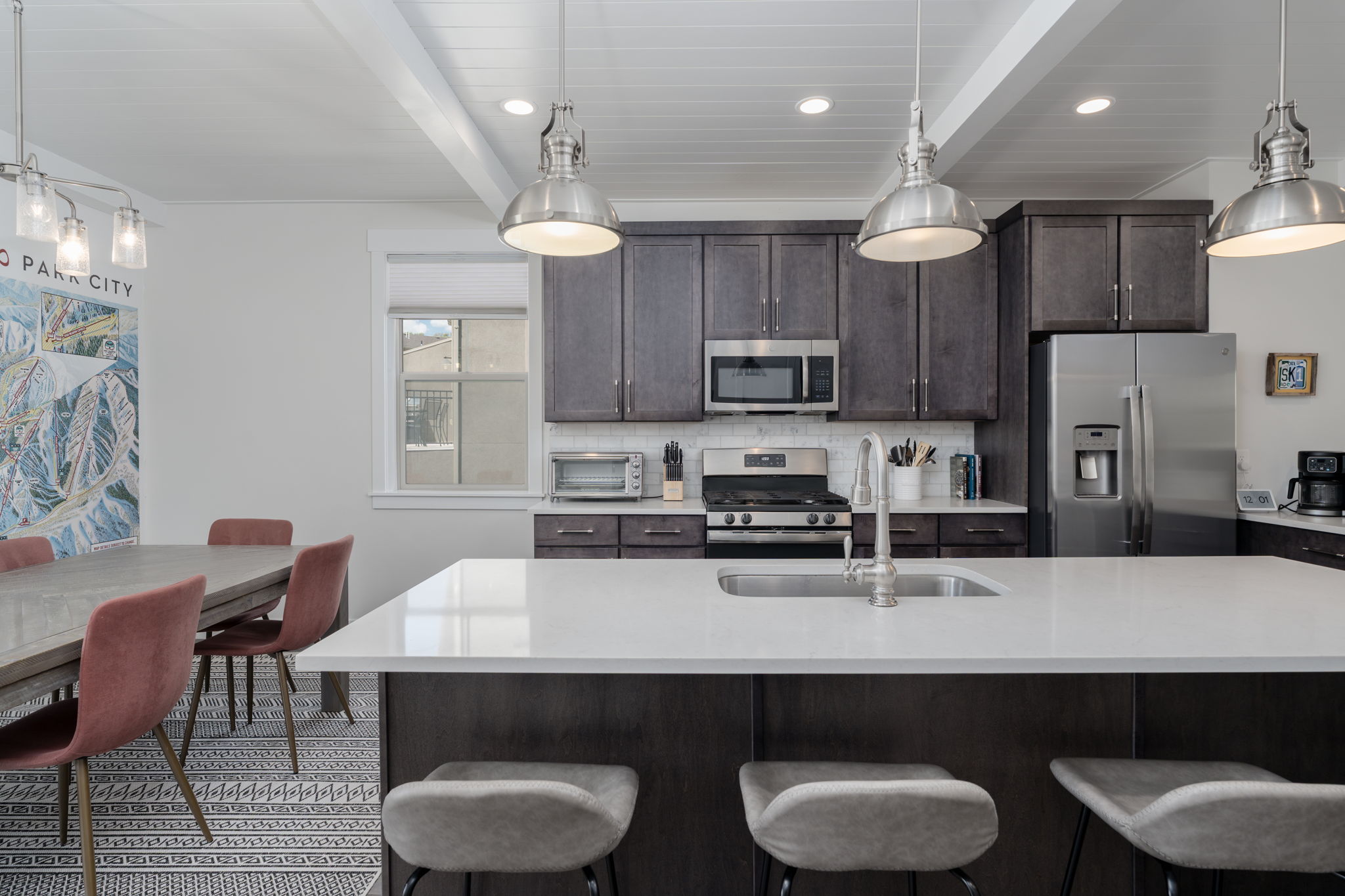 Kitchen featuring dark wood finish cabinets, beamed ceiling, stainless steel appliances, hanging light fixtures, and light stone countertops