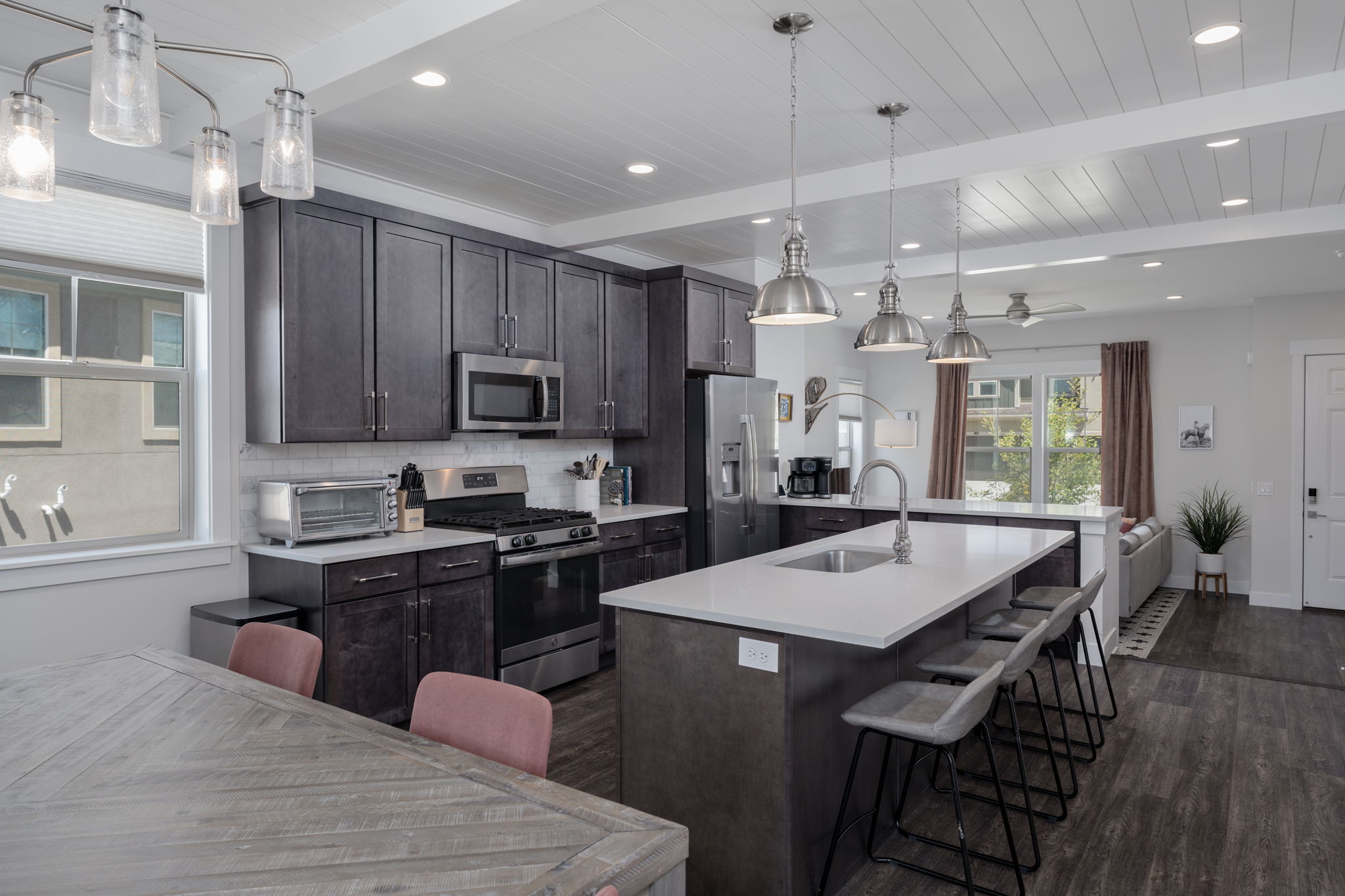 Kitchen with stainless steel appliances, a center island with sink, a kitchen bar, decorative backsplash, and dark wood-style flooring