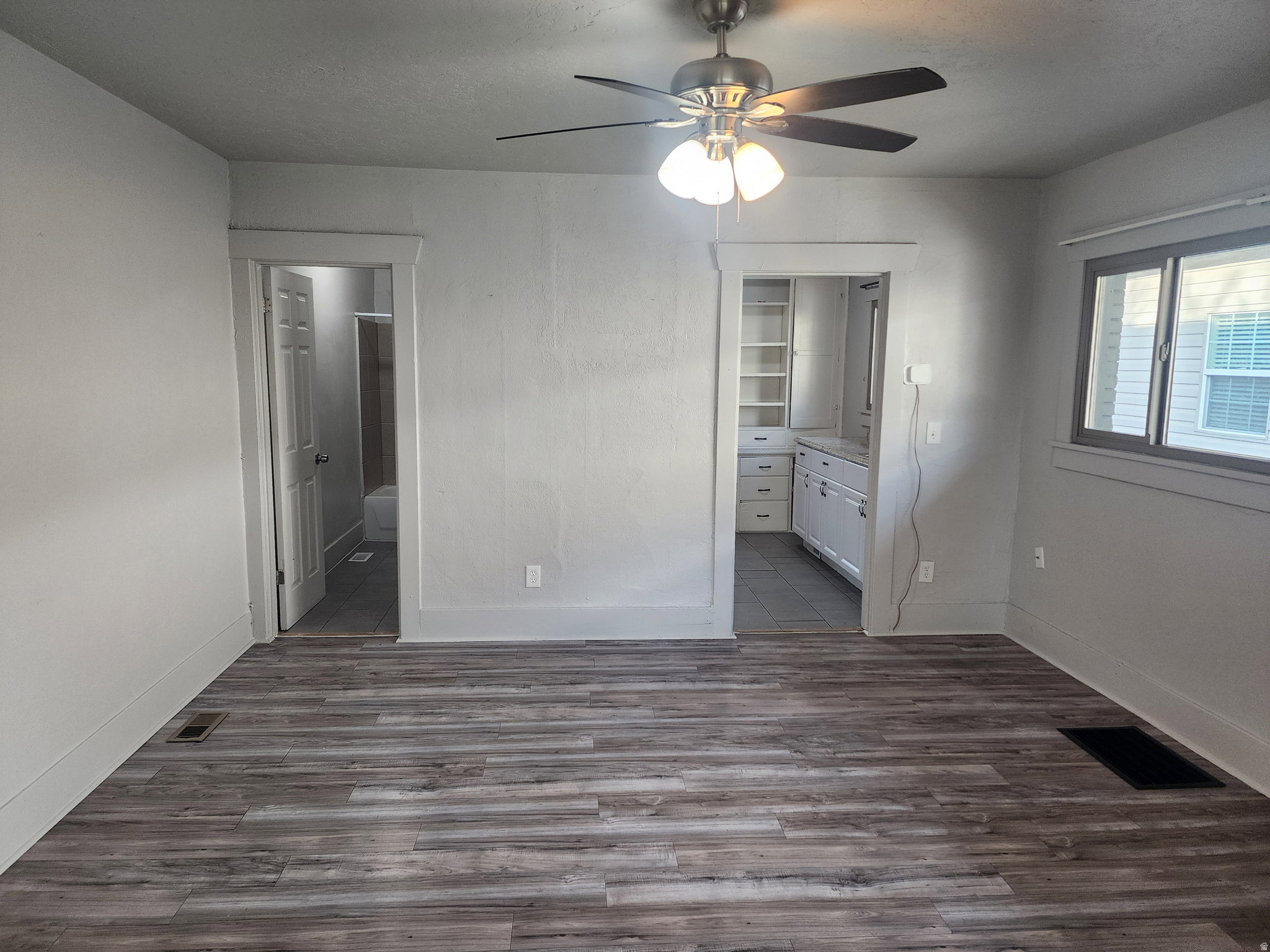 Unfurnished bedroom with ensuite bathroom, dark wood-style floors, and a ceiling fan