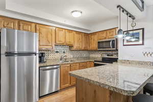 Kitchen with stainless steel appliances, a peninsula, tasteful backsplash, a kitchen breakfast bar, and light wood-style flooring