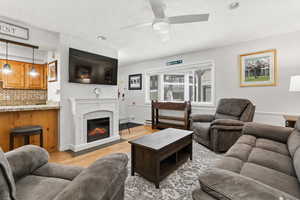 Living room with light wood finished floors, a glass covered fireplace, and ceiling fan