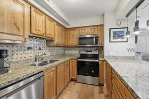 Kitchen with stainless steel appliances, light wood-style flooring, light stone countertops, backsplash, and pendant lighting