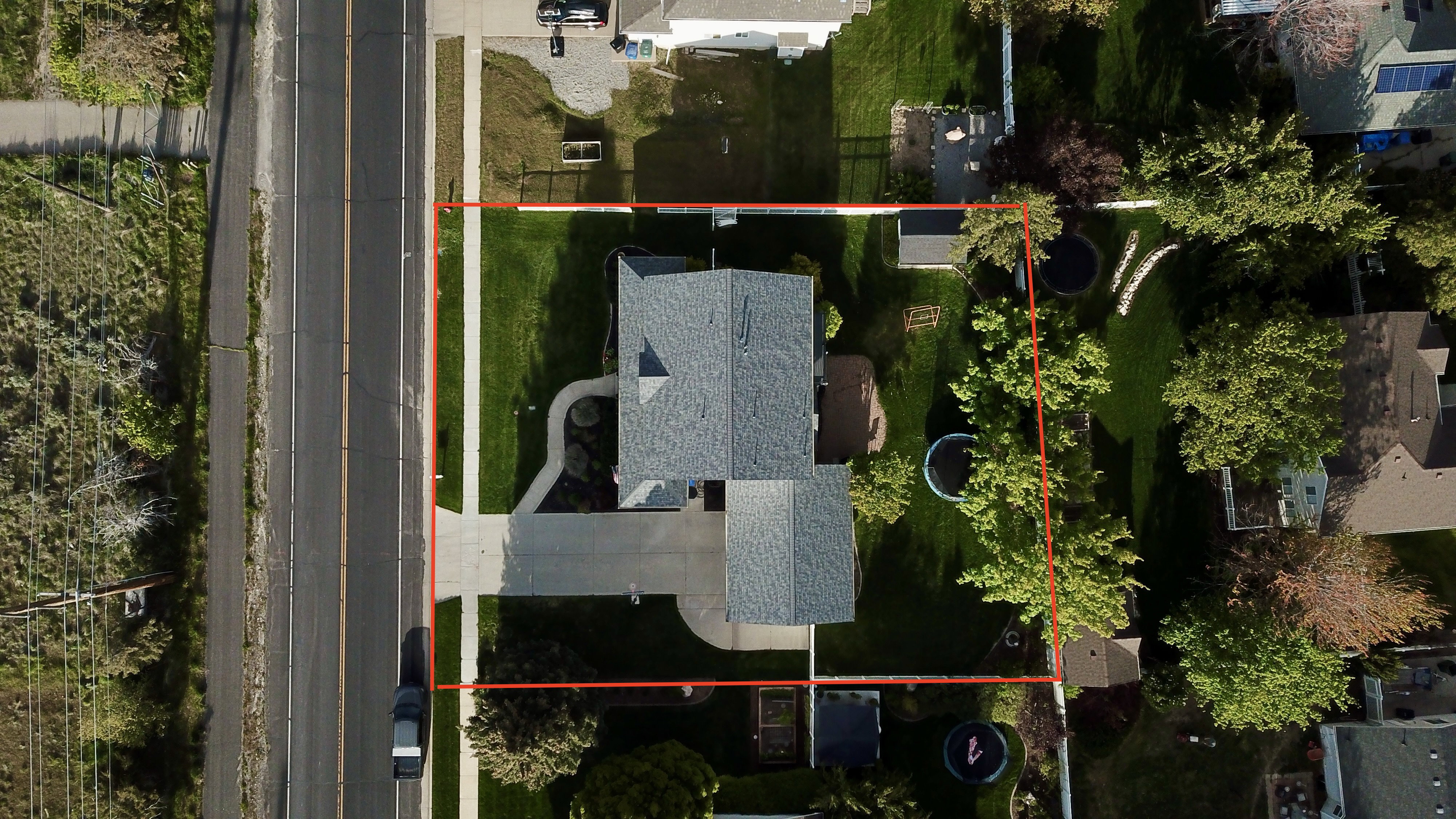 Aerial overview showcasing the property's perimeter, a gray-shingled roof, a paved driveway, and a spacious green lawn