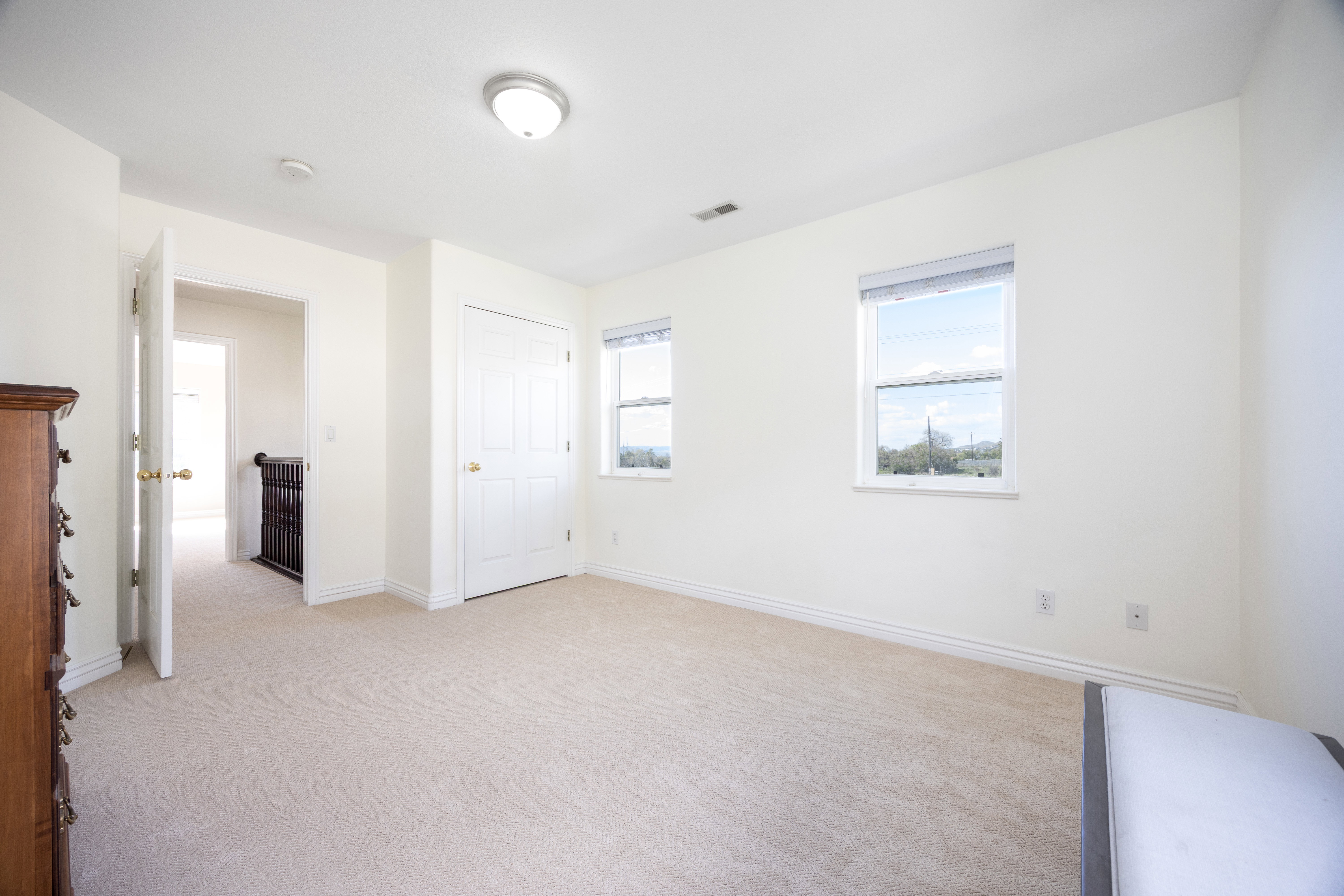 Carpeted room with two double-hung windows, a flush-mount ceiling light, a white paneled door, and white baseboards