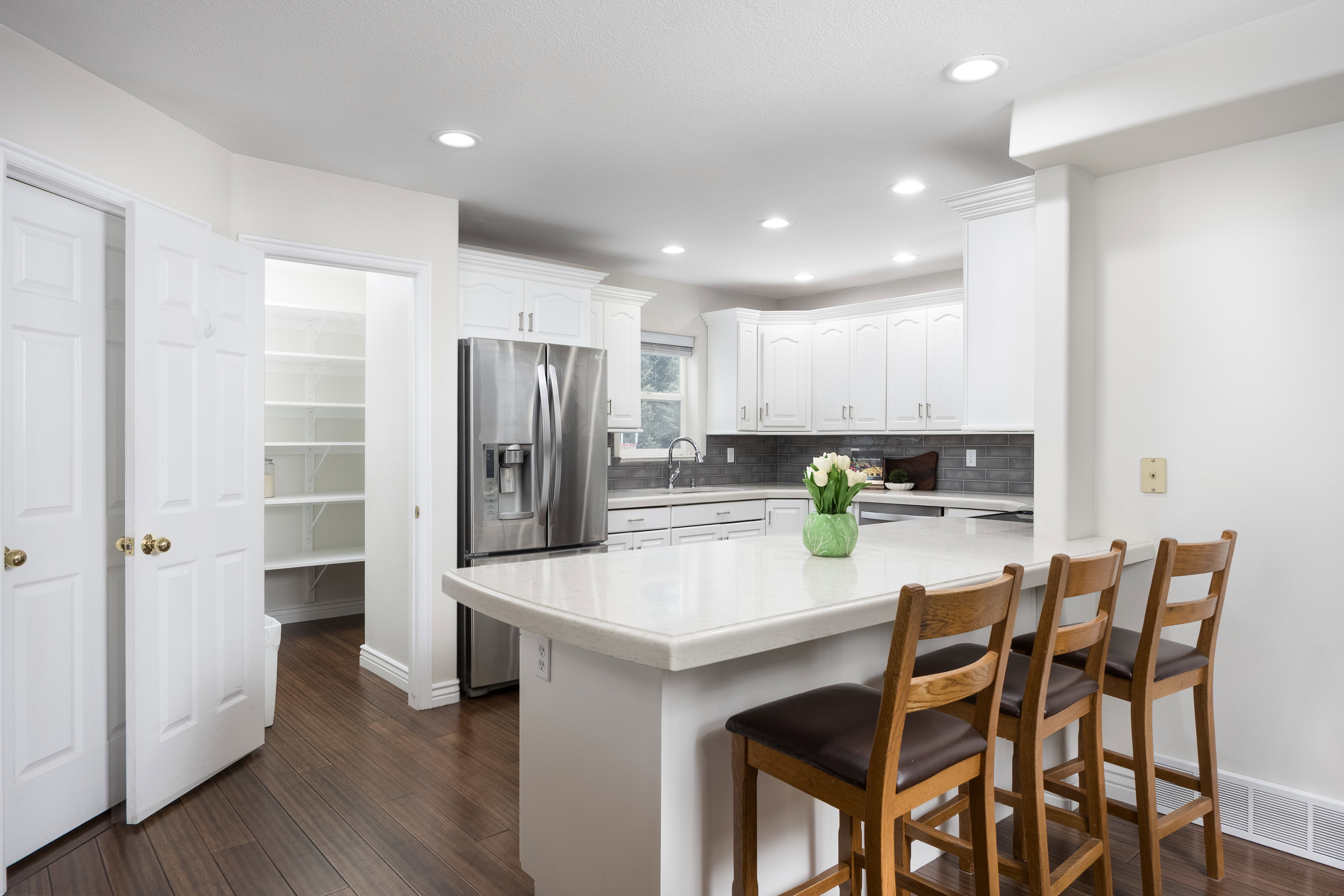White kitchen cabinetry with stainless steel appliances, a white countertop island, and dark wood-finish flooring