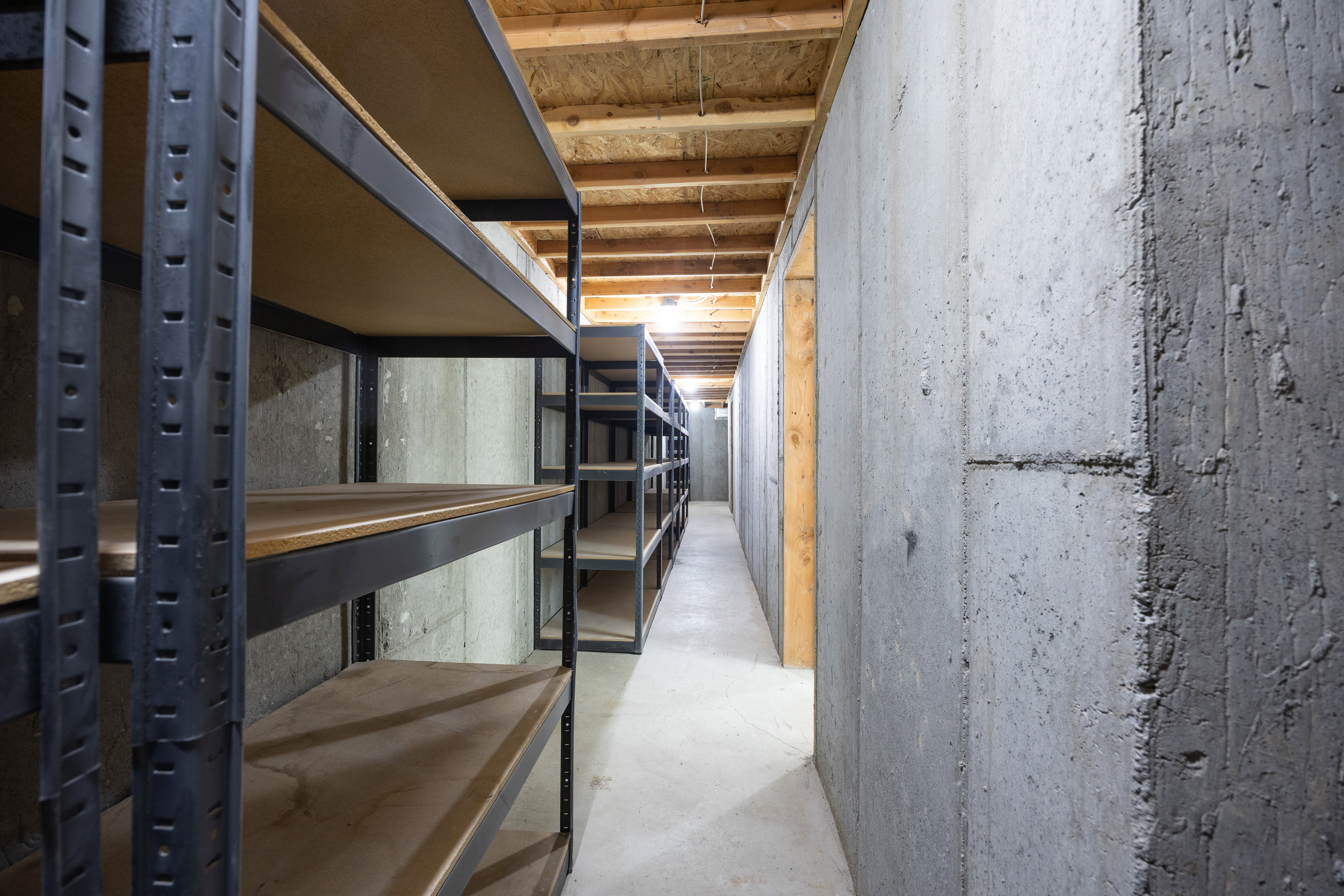 Basement storage area featuring extensive metal shelving, exposed concrete walls, an unfinished wood ceiling, and concrete flooring