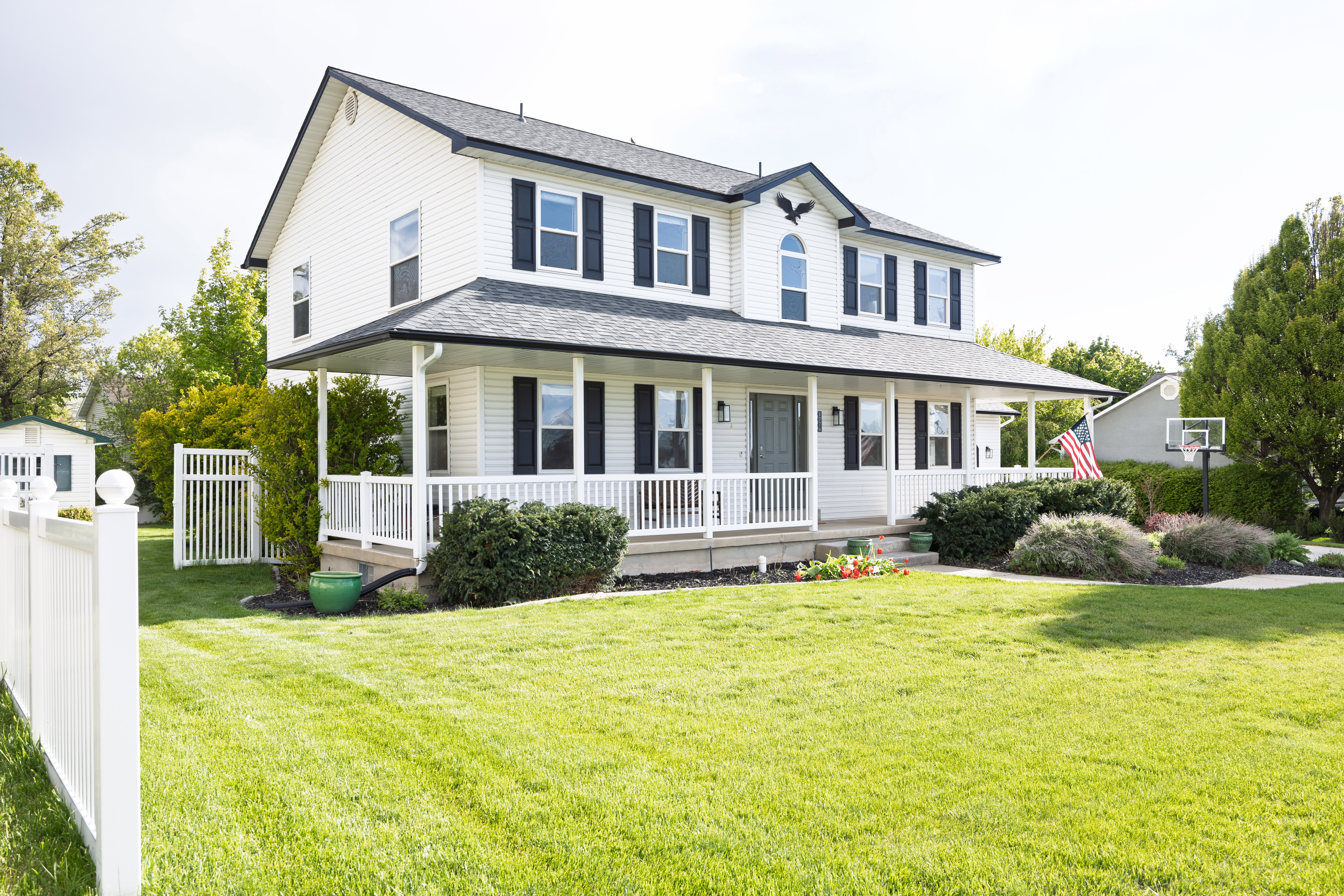 Two-story home featuring a full-width covered porch, white vinyl siding, dark shutters, and a well-maintained front lawn