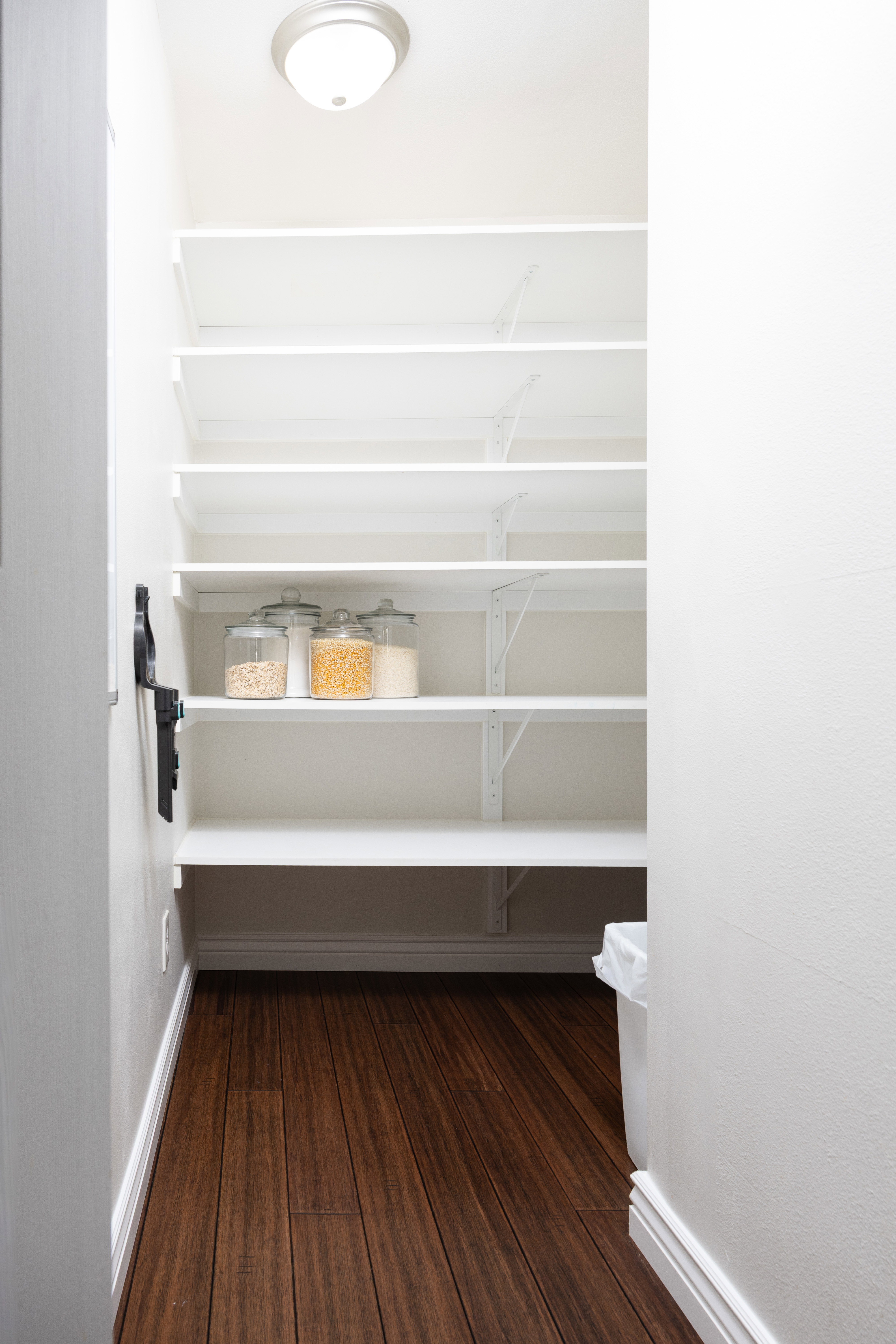 Expansive pantry featuring dark wood-finish flooring, white adjustable shelving, a flush-mount ceiling light fixture, and white baseboards