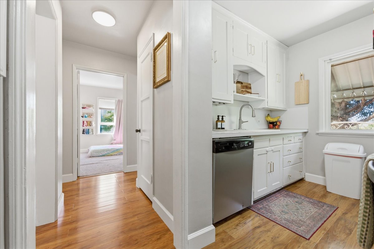 Kitchen with light wood-style flooring, light countertops, white cabinets, dishwasher, and open shelves
