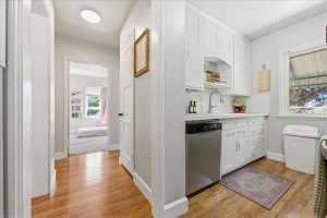 Kitchen with light wood-style flooring, light countertops, white cabinets, dishwasher, and open shelves