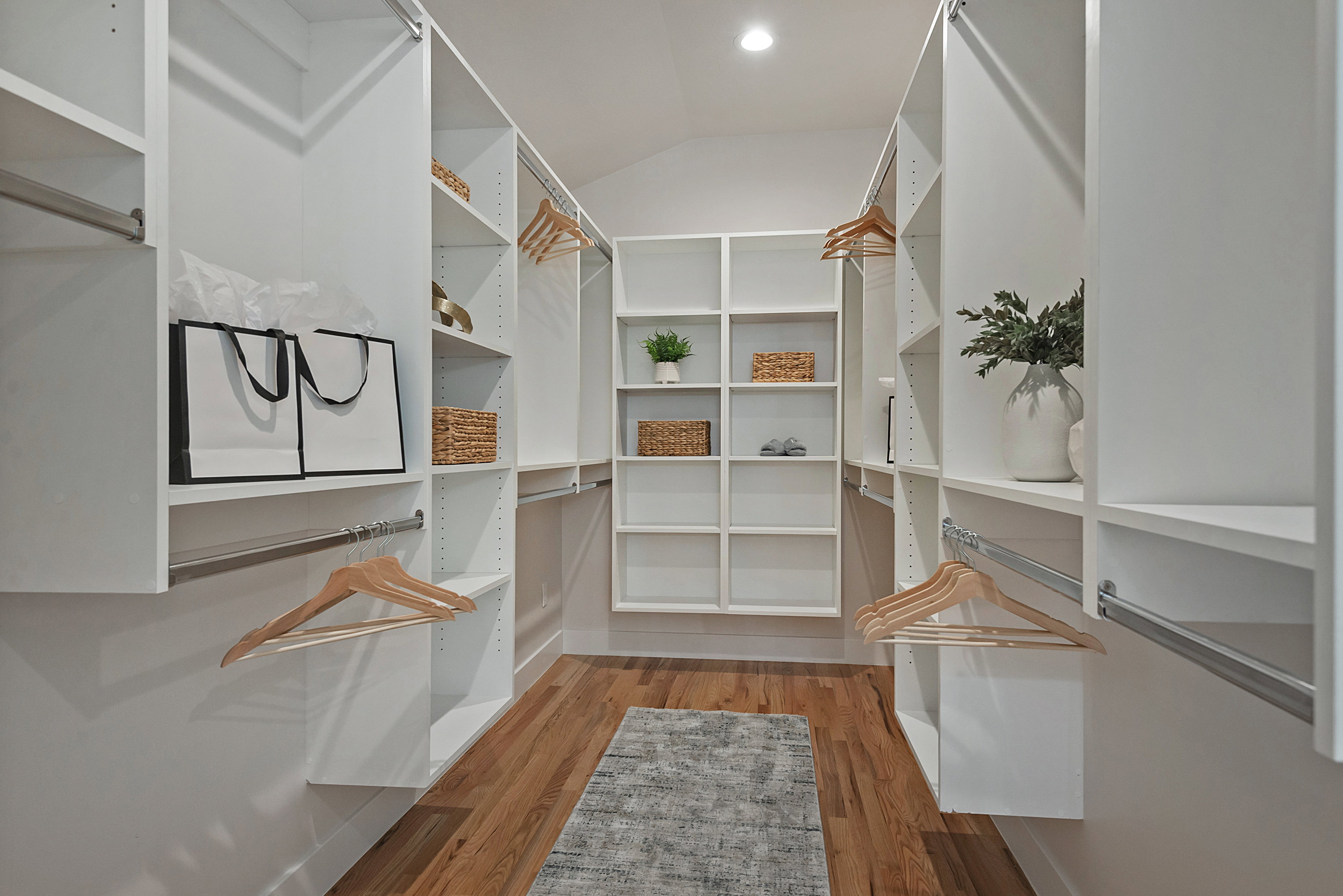 Huge primary walk in closet with light wood finished floors and vaulted ceiling
