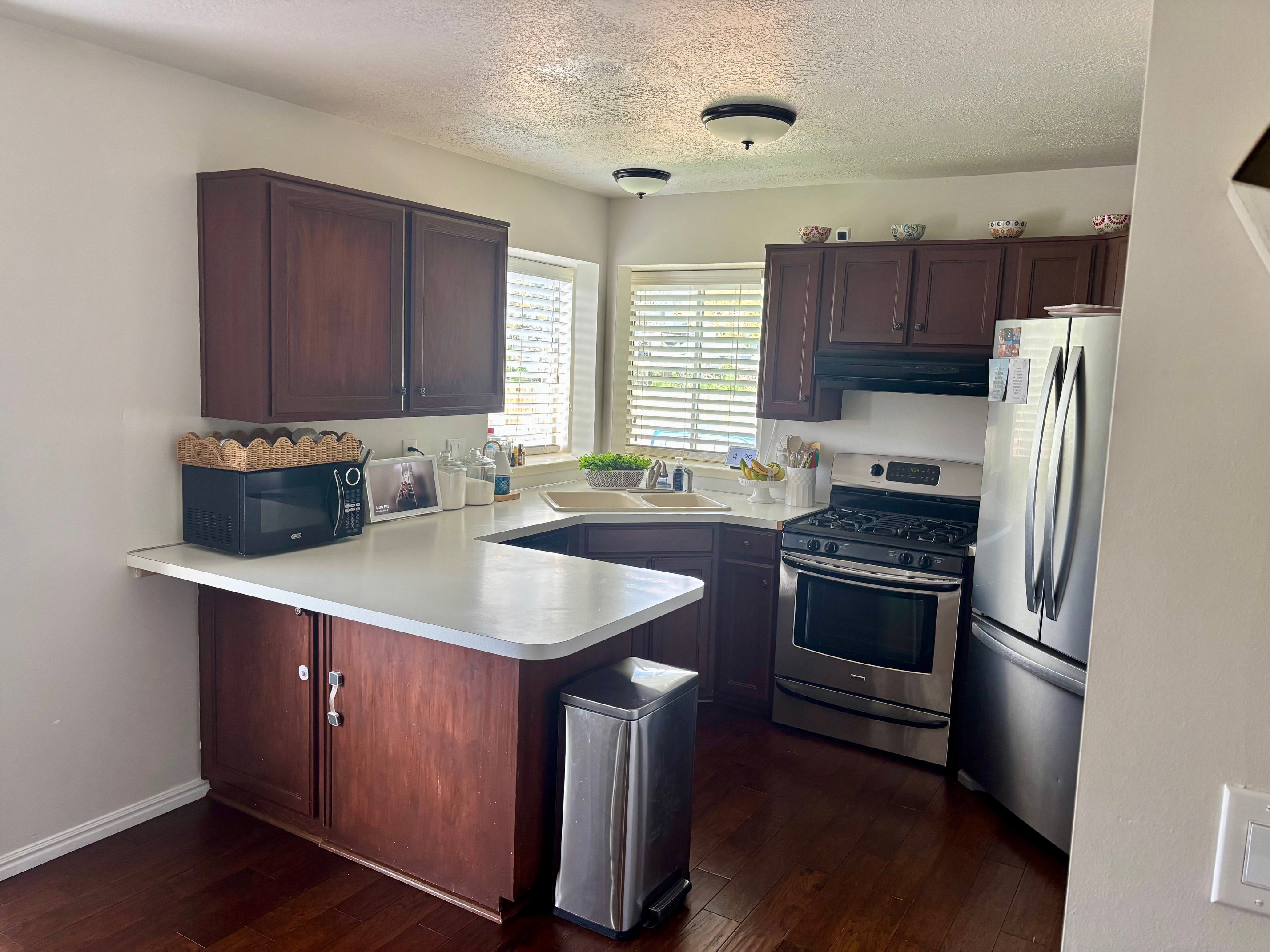 Kitchen featuring dark wood-finish cabinetry, light countertops, wood-finish flooring, a stainless steel gas range, and a stainless steel refrigerator