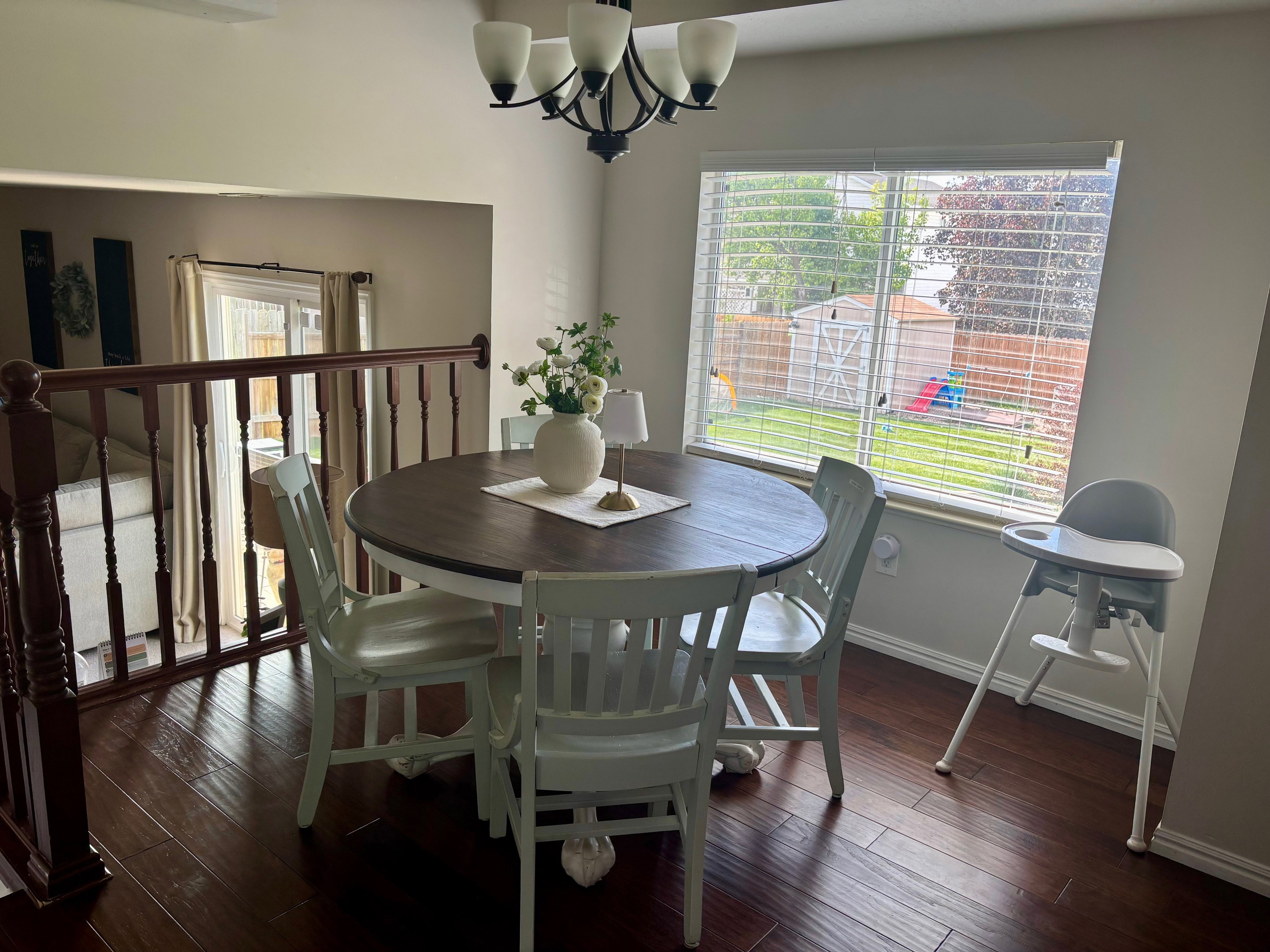 Dining area featuring wood-finish flooring, a contemporary chandelier, and a large window overlooking the backyard