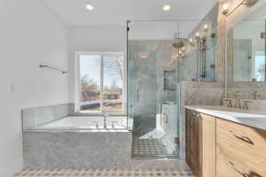 Bathroom featuring a built-in tub with a window, a glass-enclosed shower with multiple showerheads, a wood-finish vanity with a white countertop, and a mirrored medicine cabinet
