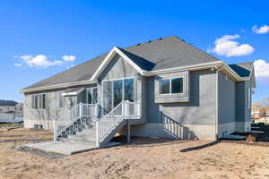 Rear exterior featuring stucco siding, a multi-level deck with white railings, sliding glass patio doors, and a ground-level concrete pad