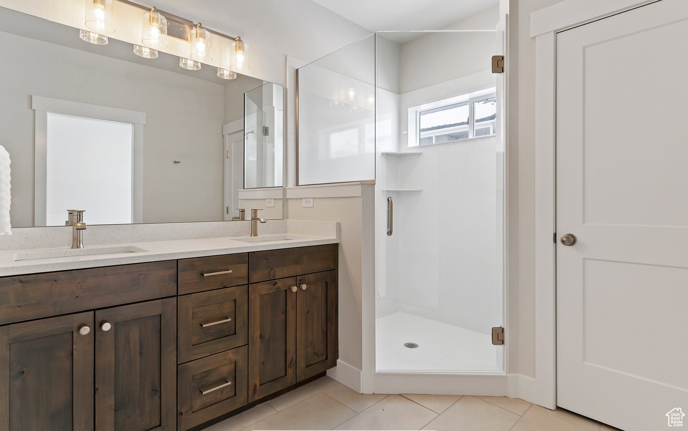 Full bathroom featuring double vanity, a stall shower, and light tile patterned floors