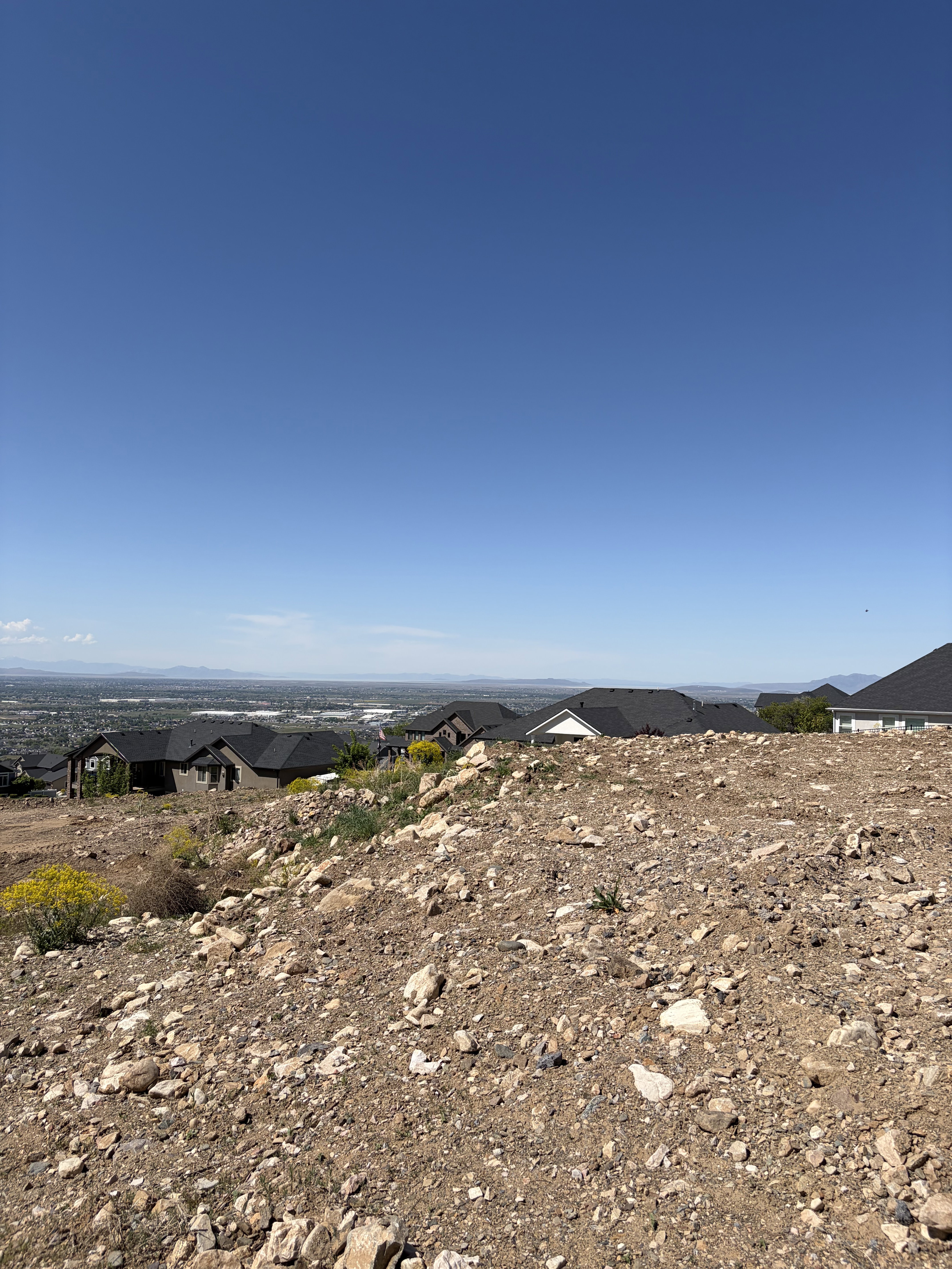 Elevated building lot featuring a clear blue sky, distant mountainous terrain, and surrounding residential structures