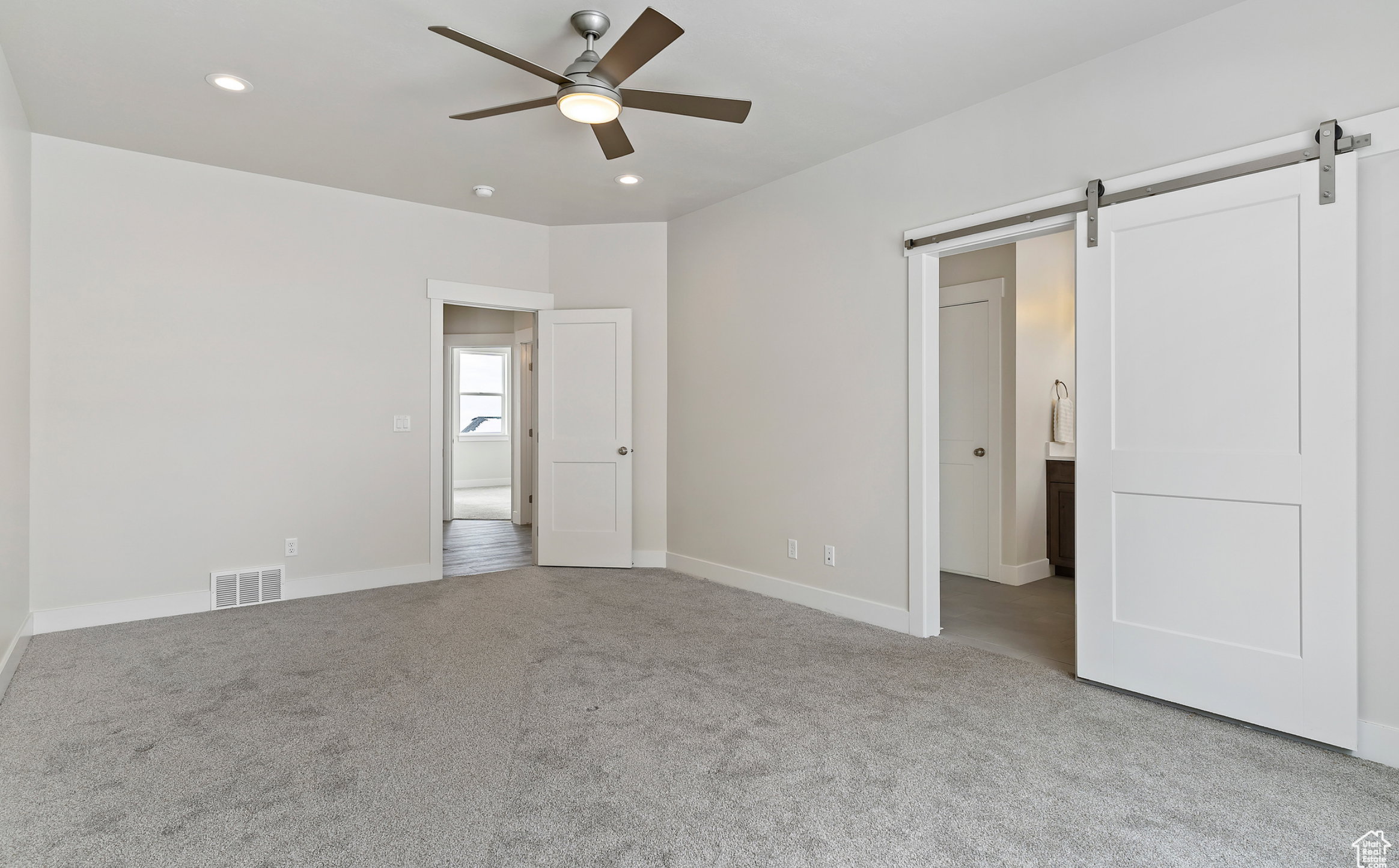 Unfurnished bedroom with a barn door, light colored carpet, recessed lighting, connected bathroom, and ceiling fan