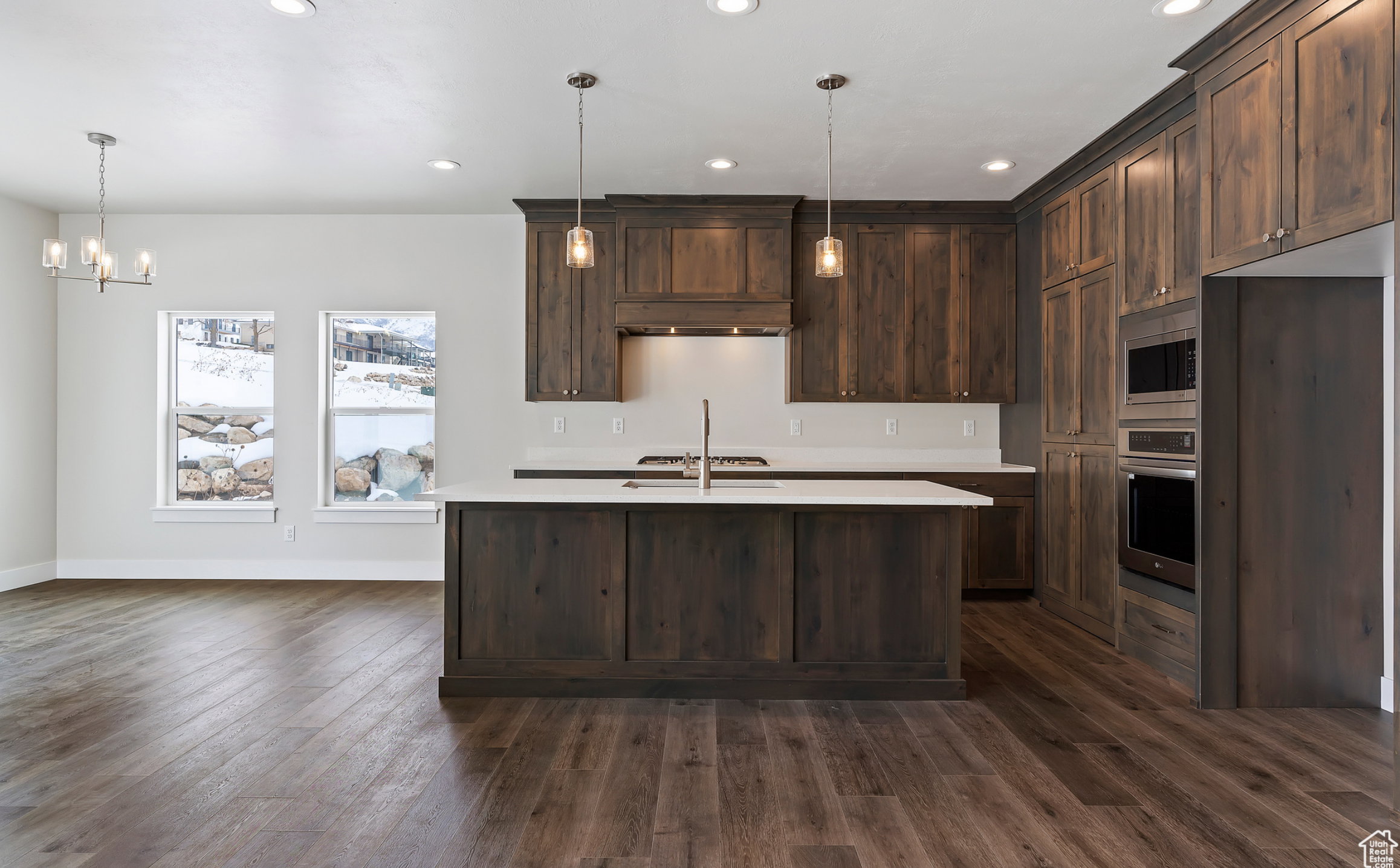 Kitchen with dark wood finish cabinetry, stainless steel appliances, a chandelier, and an island with sink