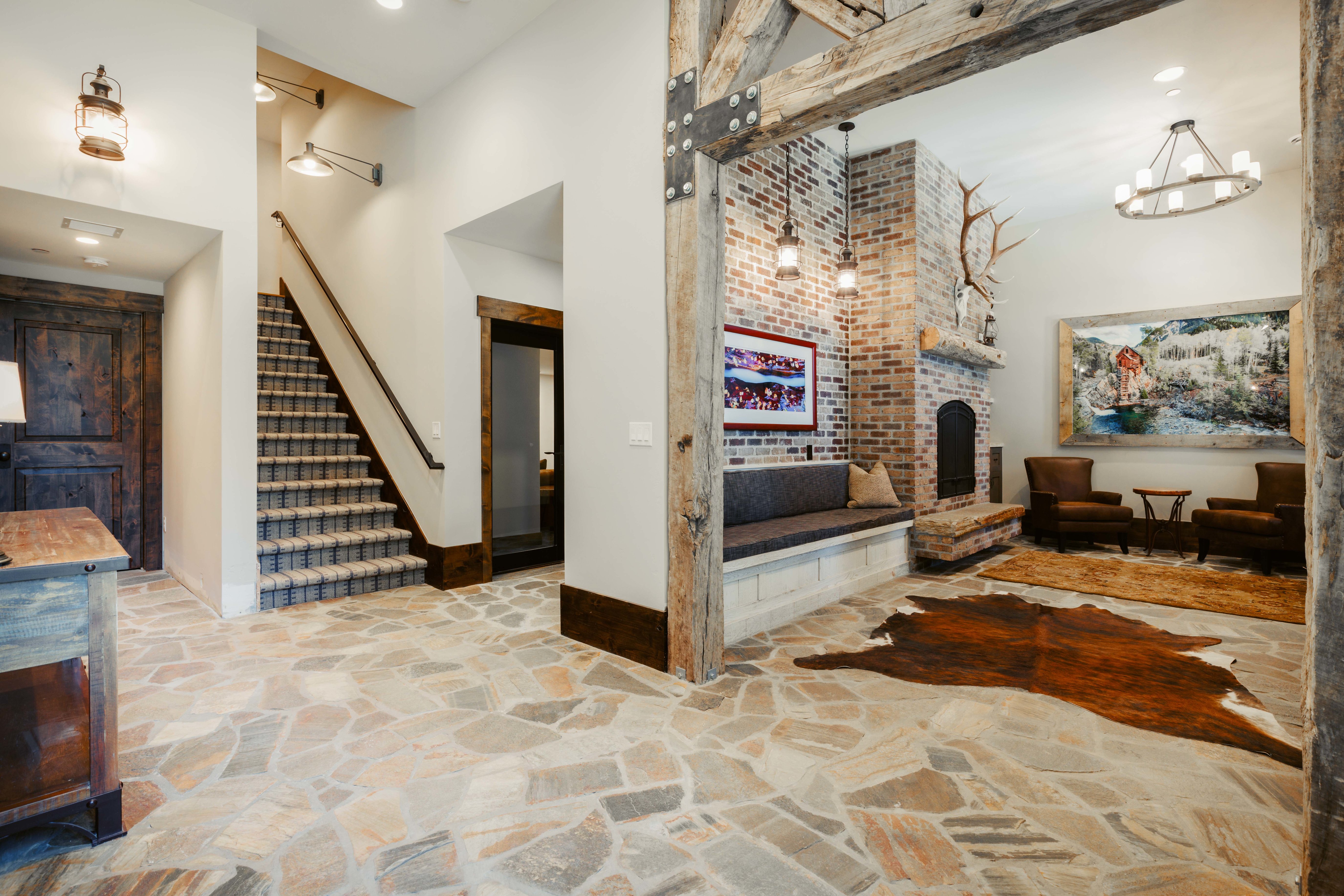 Expansive room featuring irregular flagstone flooring, a brick fireplace with stone hearth, exposed wood beams, and a built-in bench