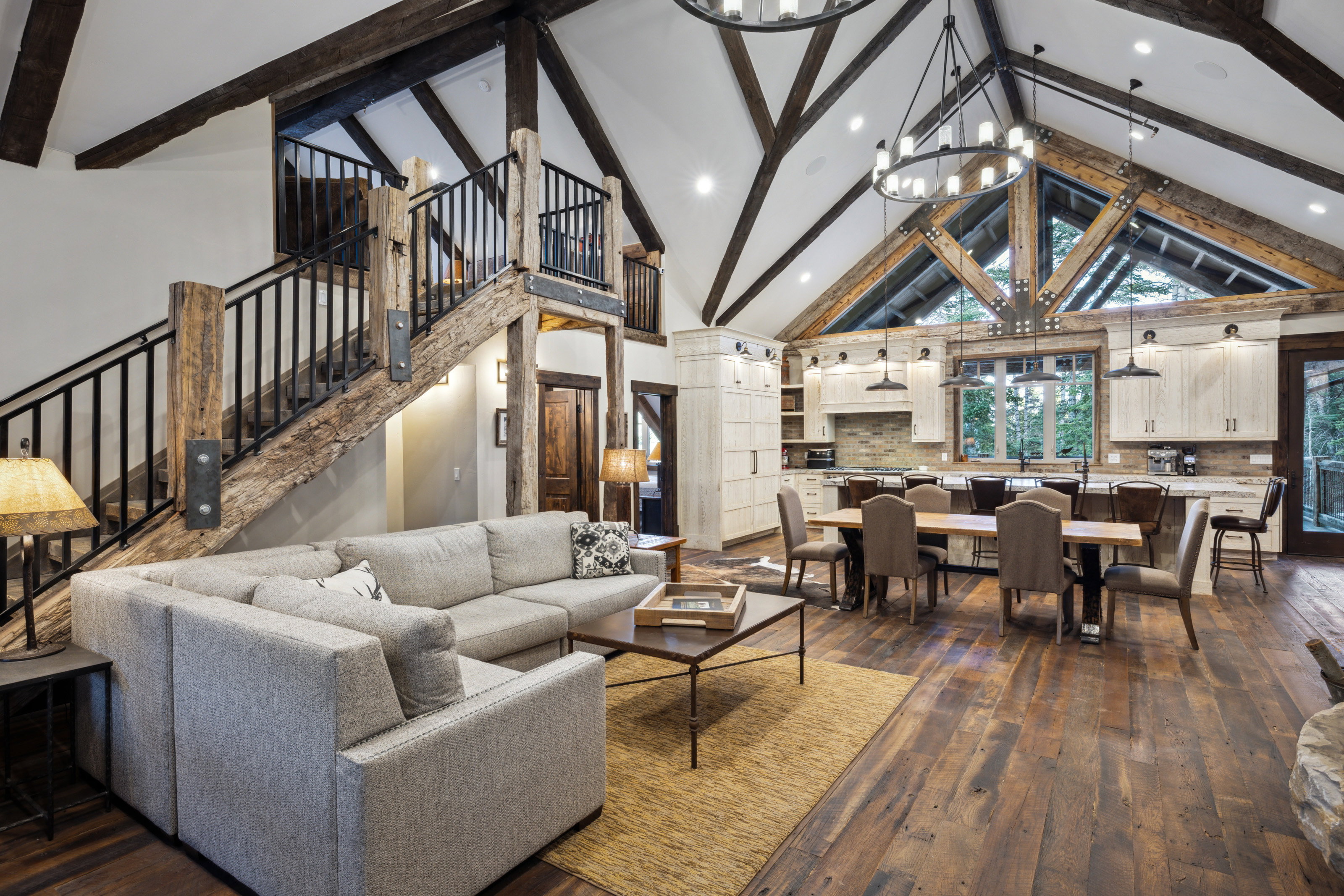 Open-concept living space featuring vaulted ceilings with exposed wood beams, a prominent staircase with wood newel posts and metal balusters, and wood-finish flooring