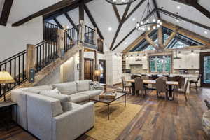 Open-concept living space featuring vaulted ceilings with exposed wood beams, a prominent staircase with wood newel posts and metal balusters, and wood-finish flooring