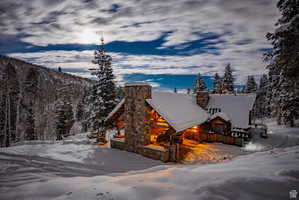 Rustic log cabin exterior featuring stone accents, a snow-covered gabled roof, and wood siding