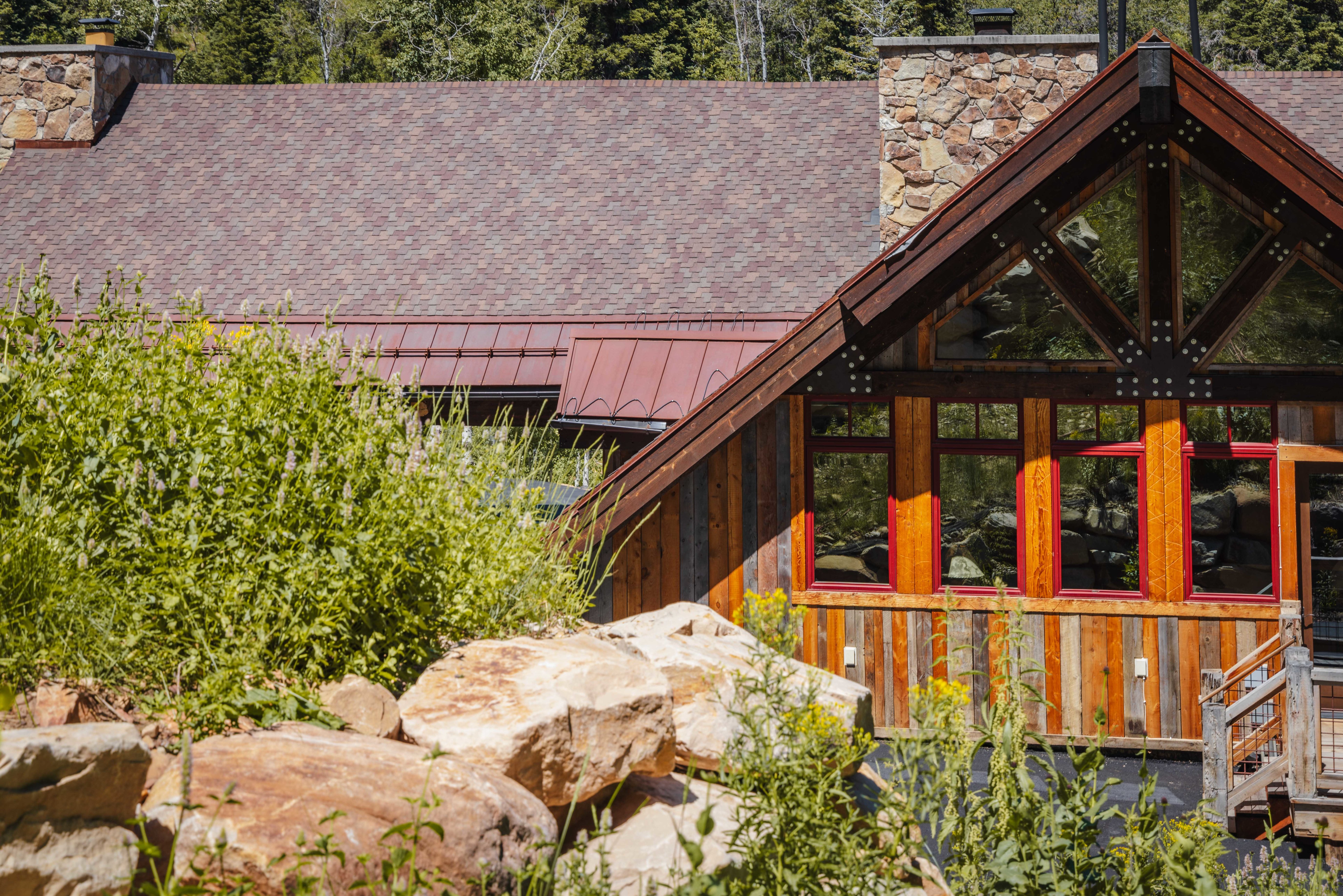 Wood-sided exterior featuring large windows with red trim and a stone chimney