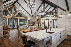 Open-concept living area featuring a vaulted ceiling with exposed wood beams, a stone fireplace, and wood-finish flooring